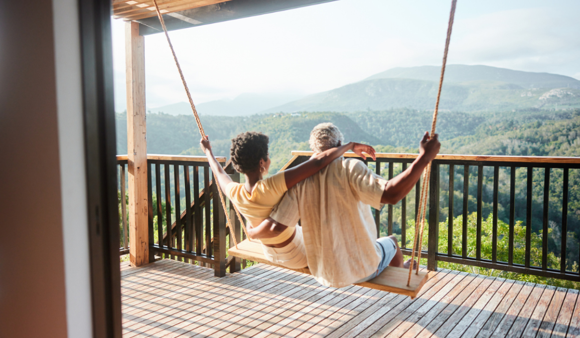 Rear view of a couple sitting together on a swing and looking at the scenic view from the balcony of their vacation rental