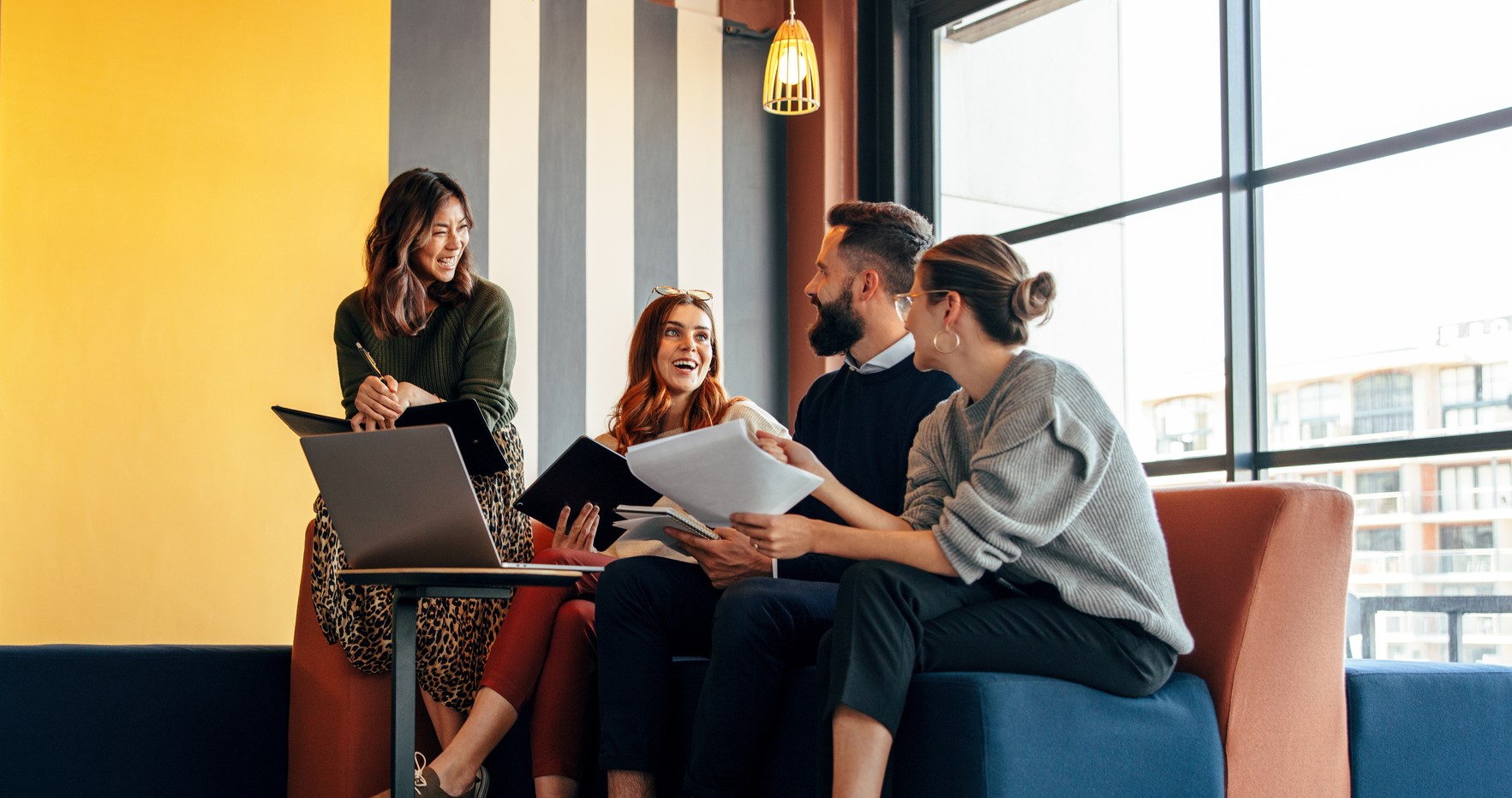 Multicultural businesspeople working in an office lobby. Group of happy businesspeople smiling while sitting together in a co-working space. Young entrepreneurs collaborating on a new project.