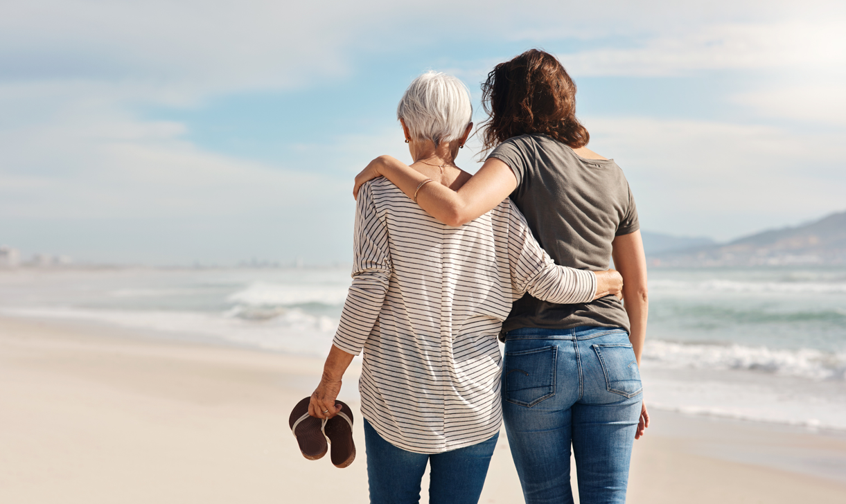 Two women walking on a beach facing the horizon